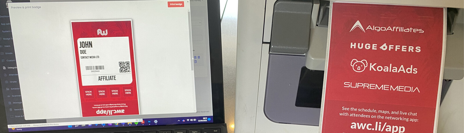 Badging software previewing a badge on a laptop beside a badge printer producing a printed badge