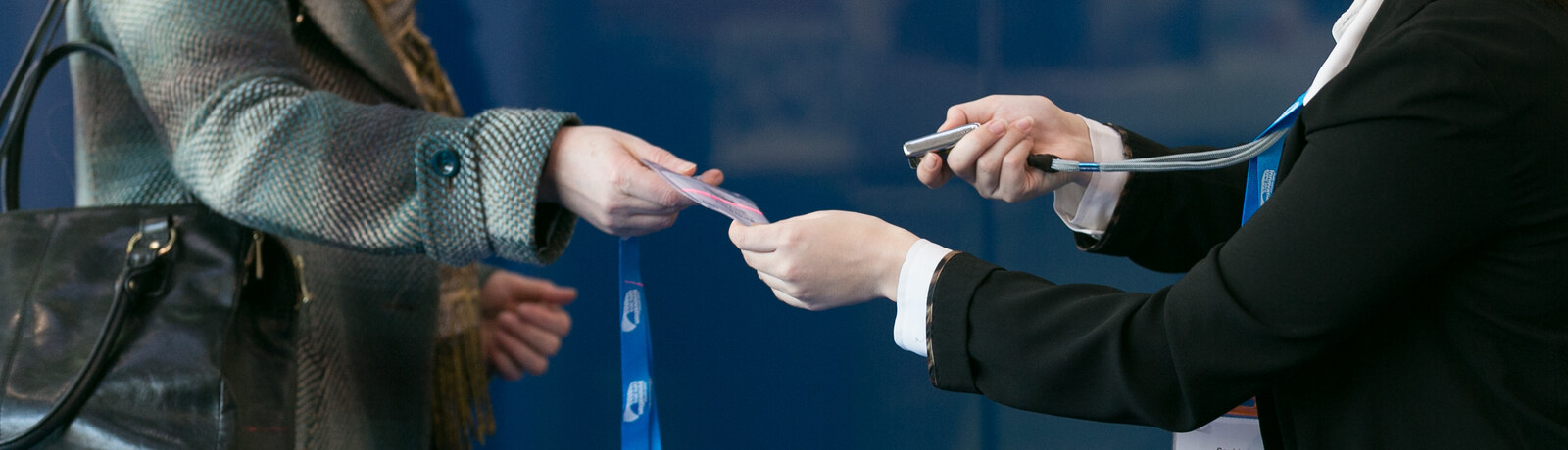 Event staff handing a printed badge and lanyard to an attendee at a registration desk
