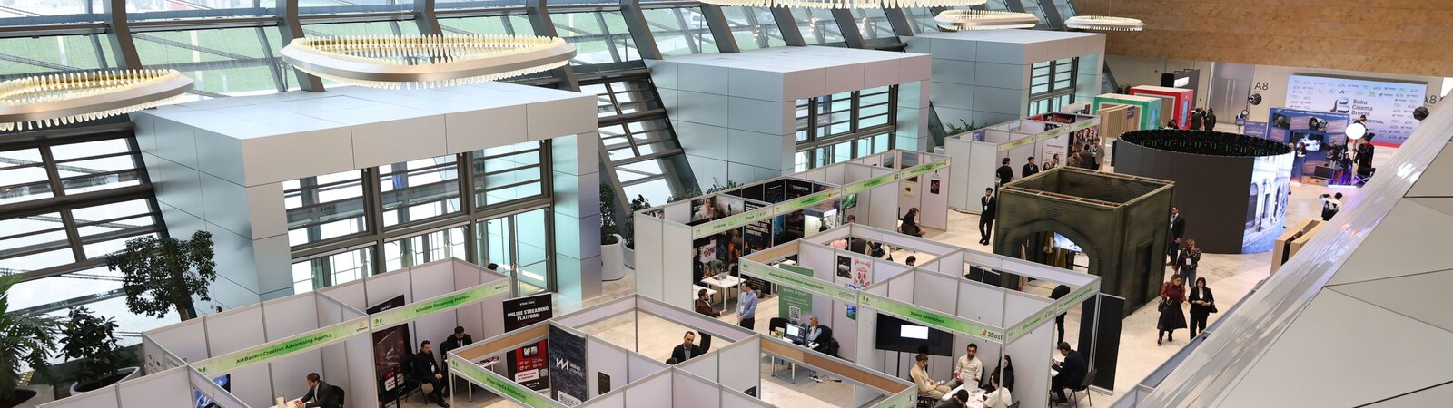 Exhibition stands and delegates across a modern trade show hall, viewed from above