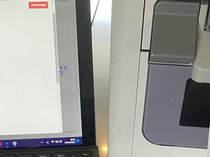 Badging software previewing a badge on a laptop beside a badge printer producing a printed badge
