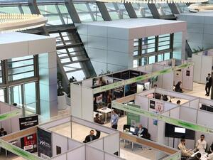 Exhibition stands and delegates across a modern trade show hall, viewed from above